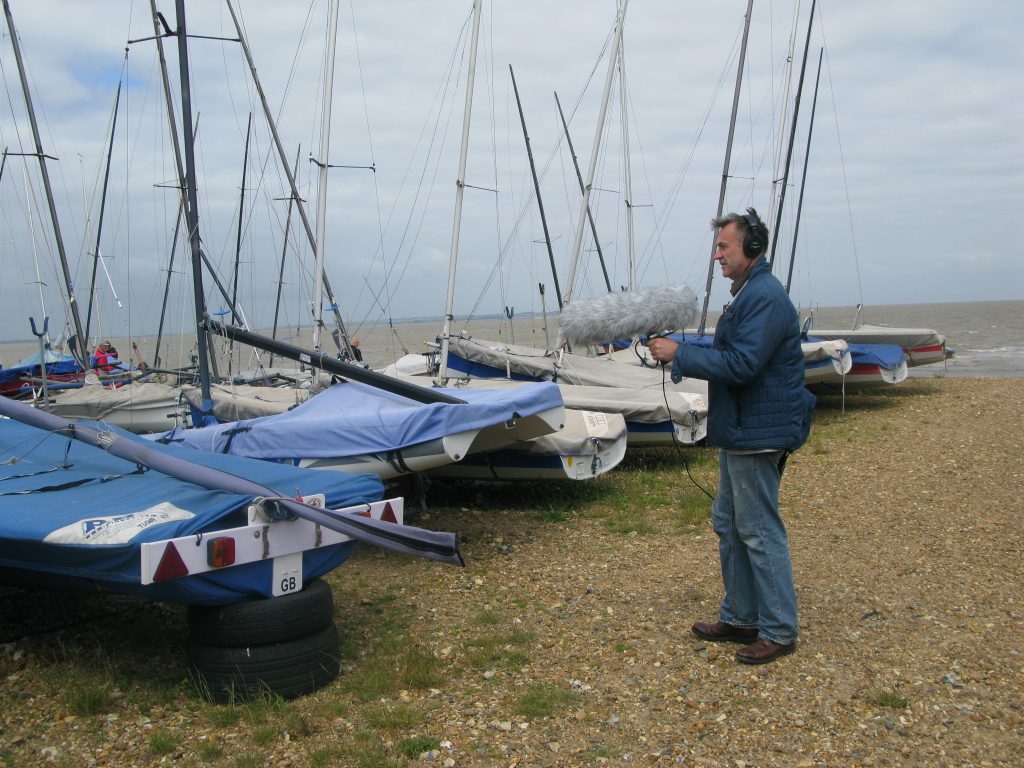 Man with headphones and microphone on a beach with boats