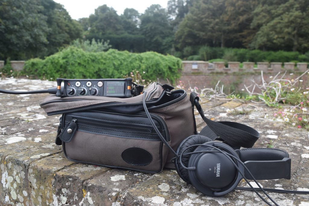 Sound devices MixPri and headphones on a wall with a verdant background - showing field recording in action.