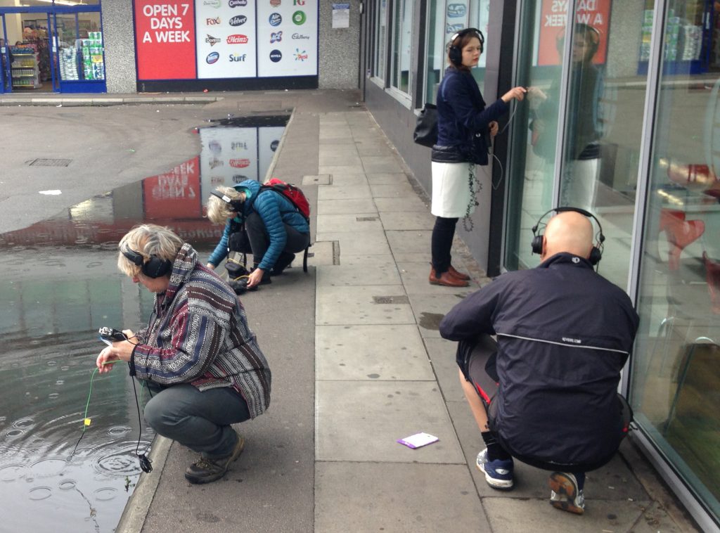 Four people with headphones making sound recordings in an urban environment.